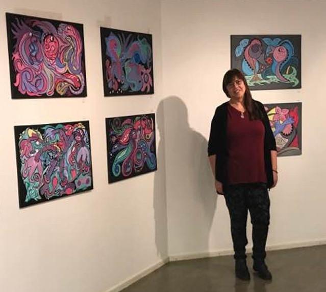 Ann-Margret Trobäck standing in front of a display wall featuring some of her acrylic art.